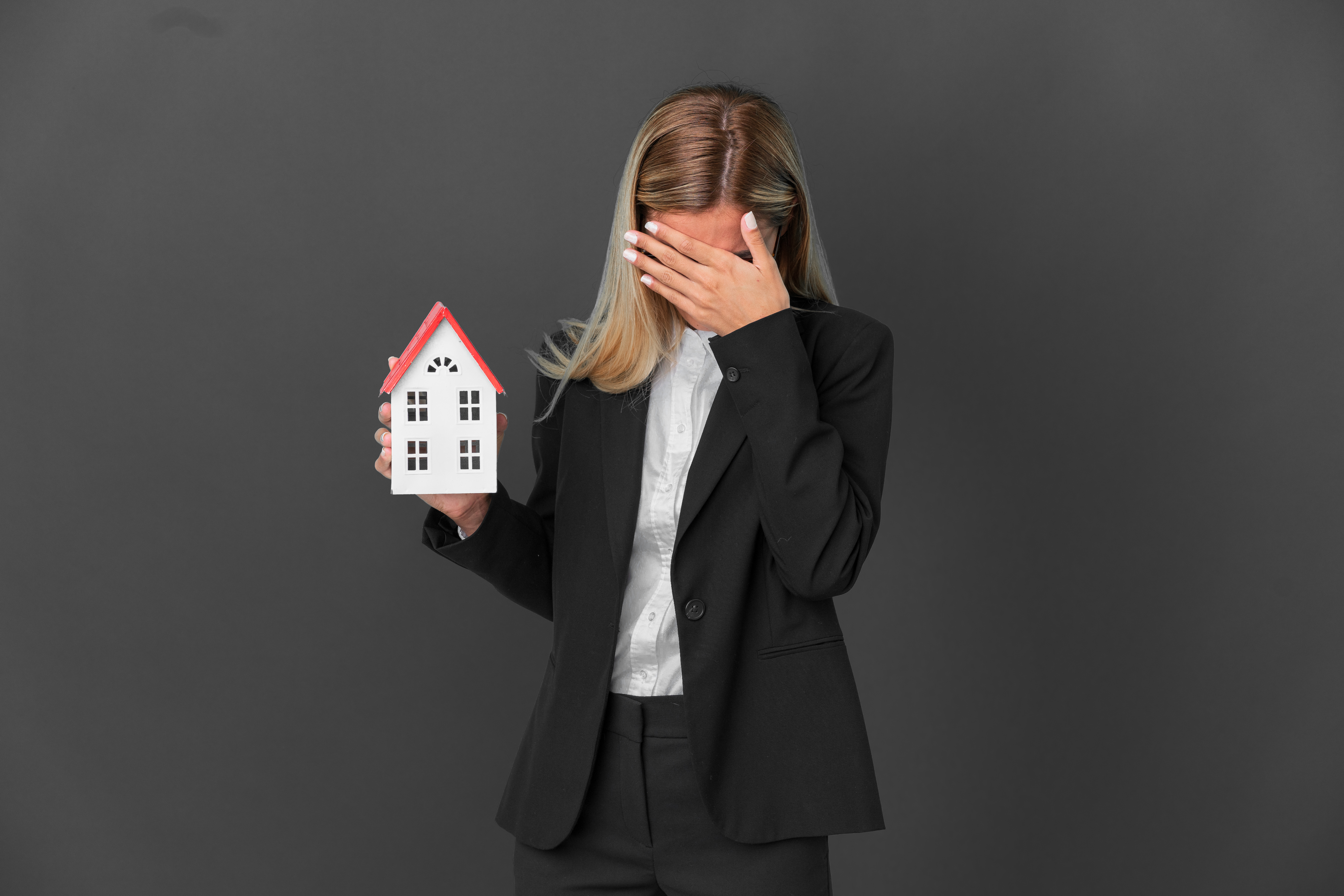 blonde uruguayan girl holding a house toy isolated on black background with tired and sick expression